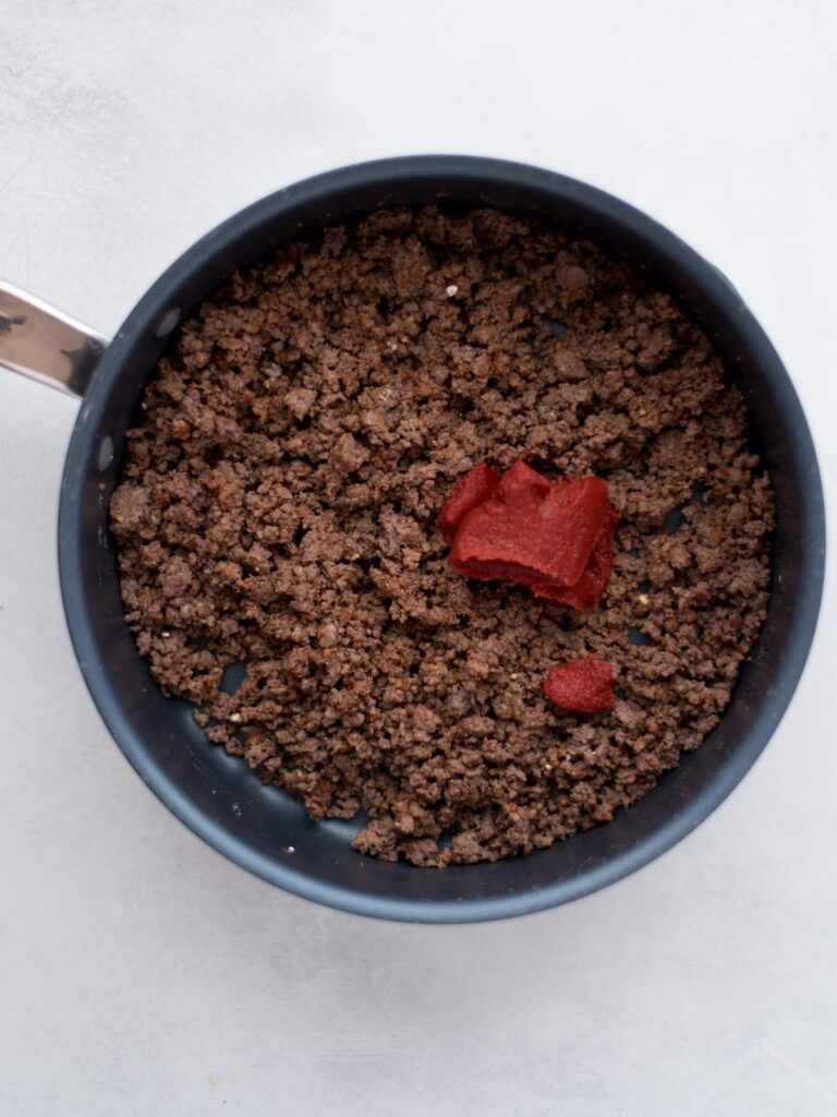 Seasoned browned ground beef with tomato paste added to the pan.