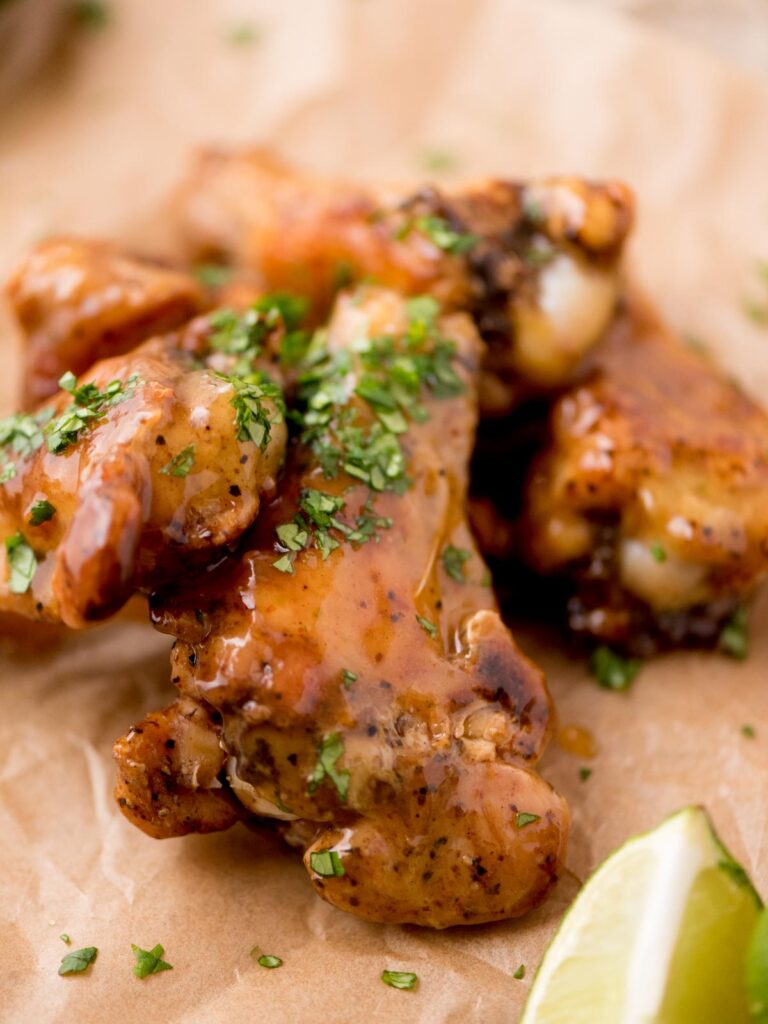 Tequila lime glazed chicken wings with chopped cilantro served on parchment paper with a lime wedge.