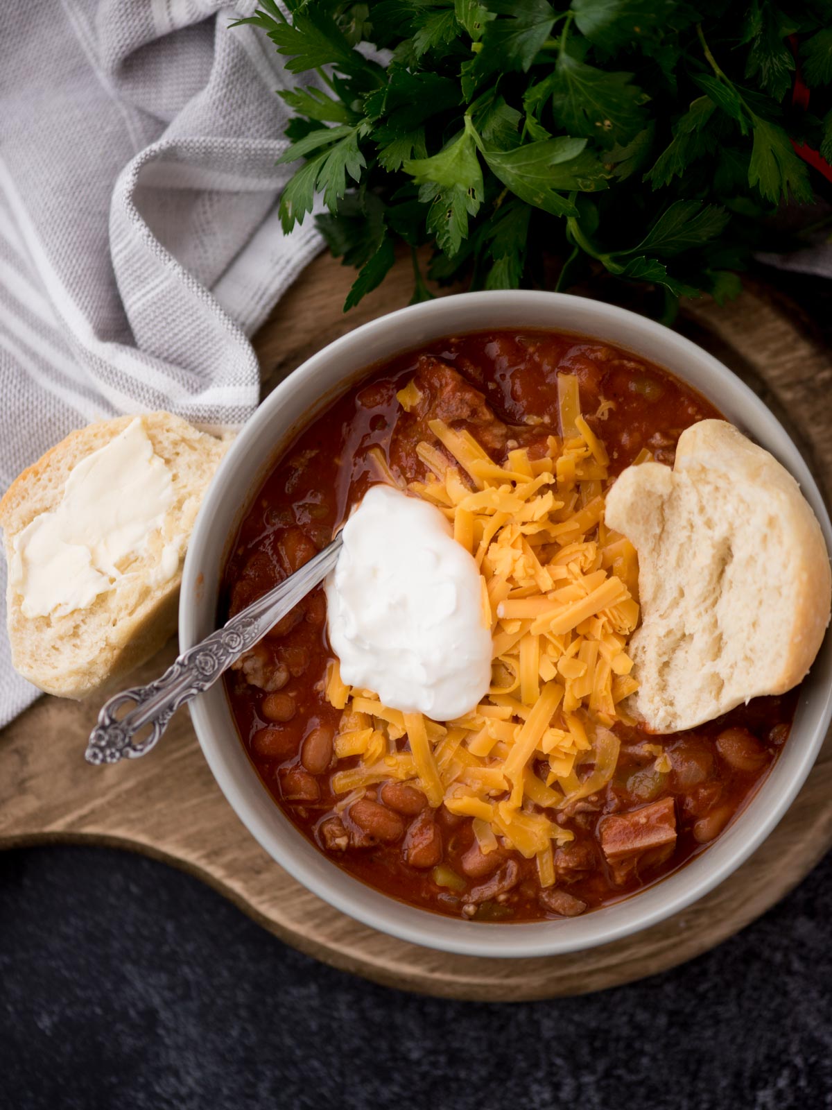 brisket chili in a grey bowl topped with shredded cheddar, sour cream, and half of a buttered roll