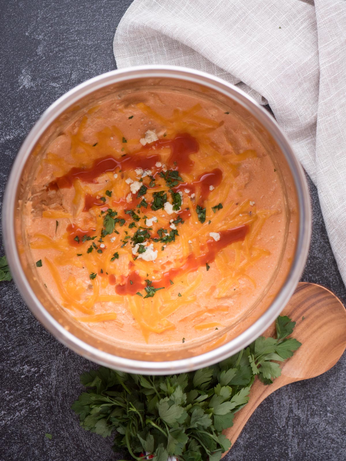 Wooden spoon resting next to a bowl of buffalo chicken dip with chopped cilantro and cheese crumbles over the top.