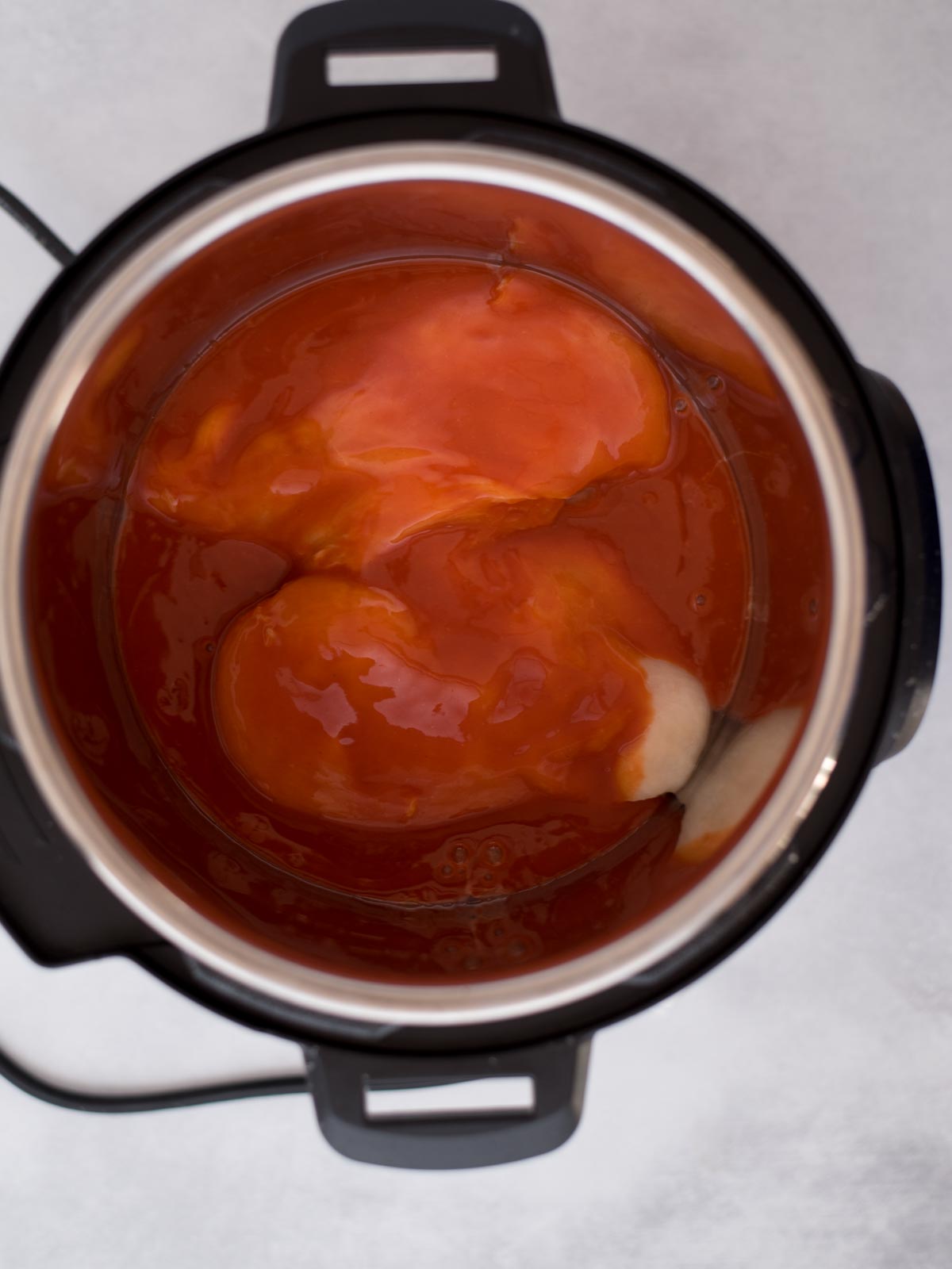 Buffalo sauce and raw chicken breasts inside the instant pot ready to cook.