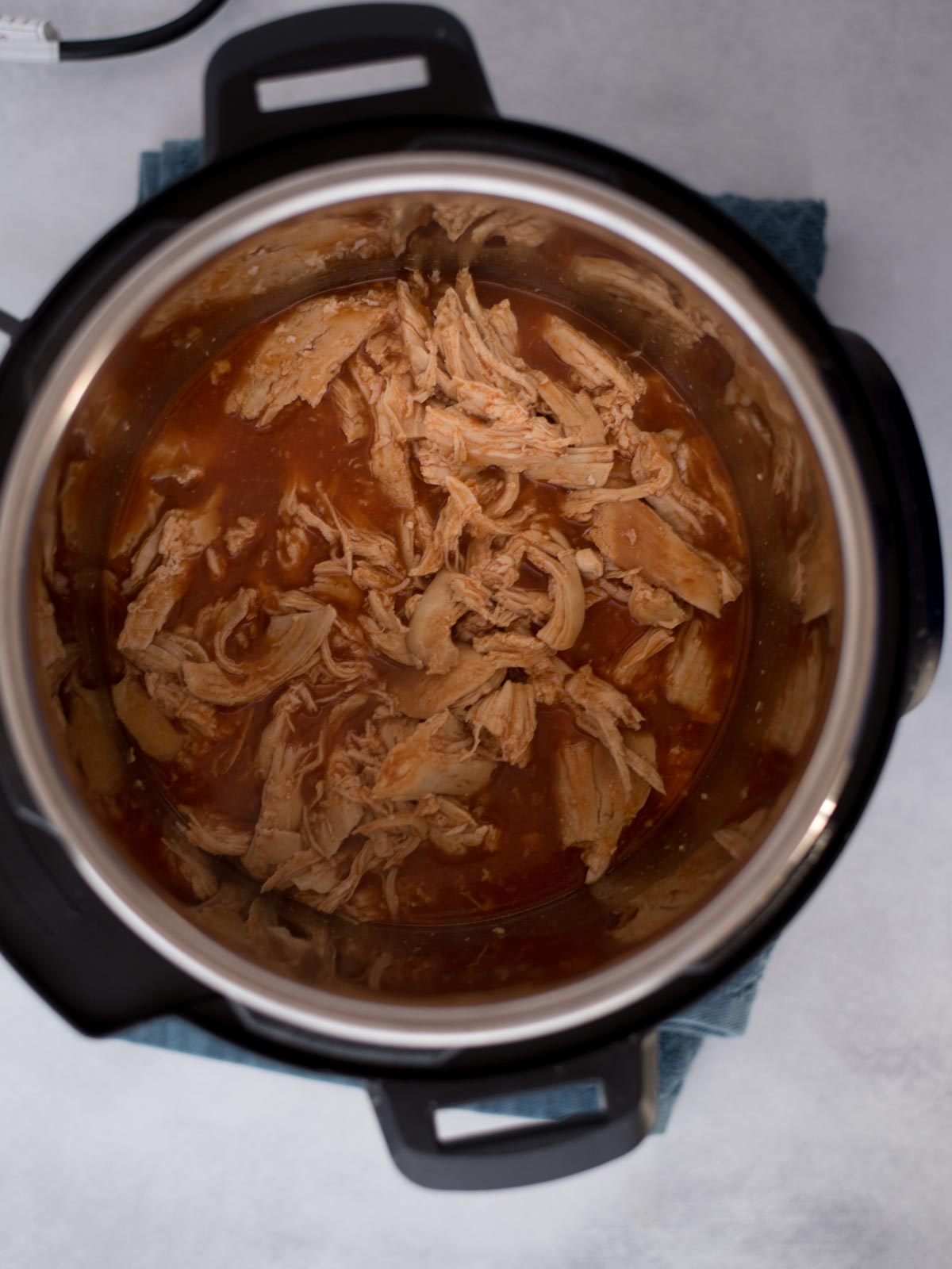 Shredded chicken inside the instant pot with buffalo sauce.