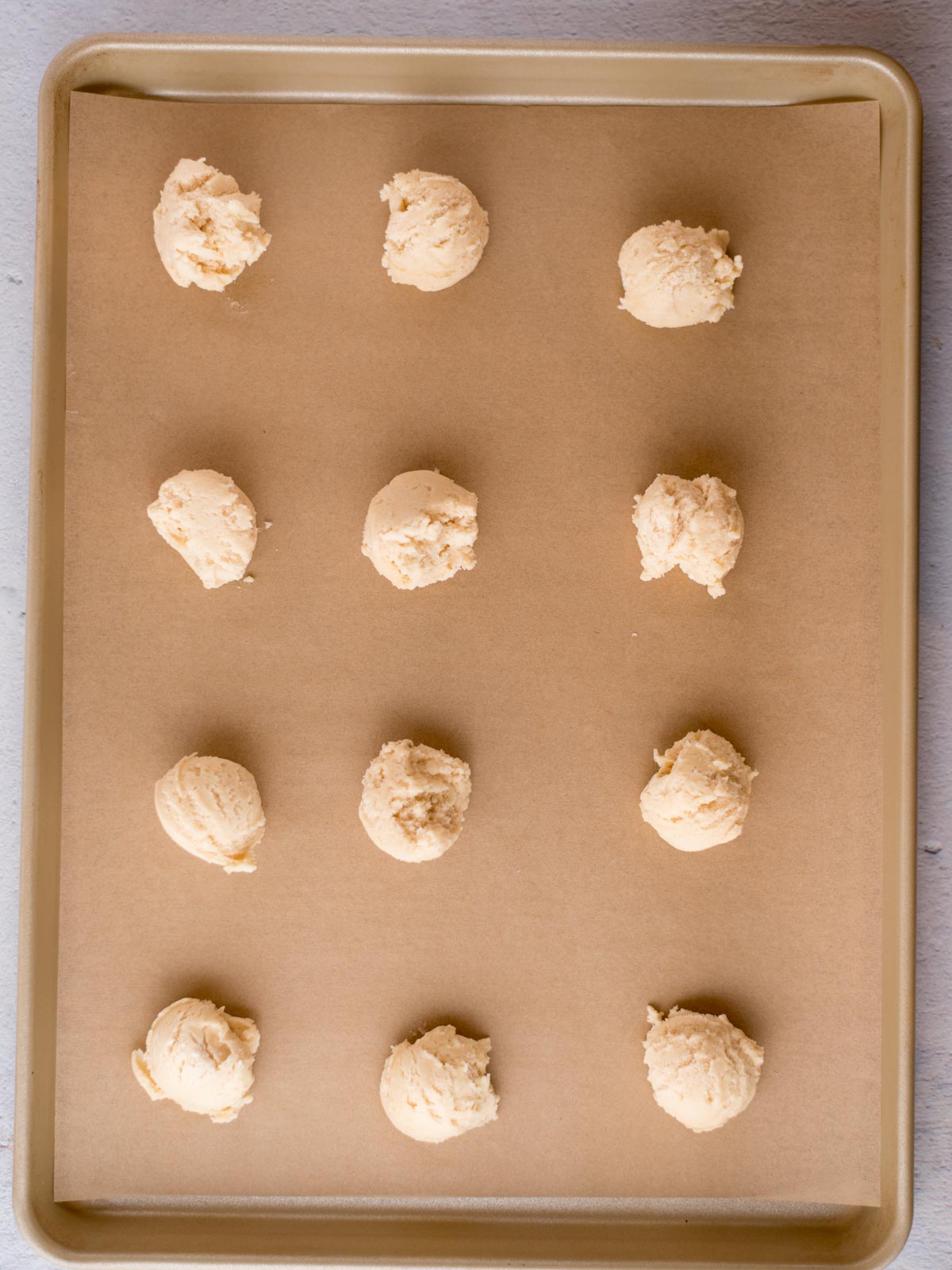 scooped balls of condensed milk cookie dough on a parchment lined baking sheet