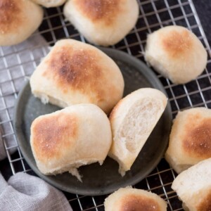 homemade yeast rolls on a plate that is resting on a cooling rack next to a kitchen towel