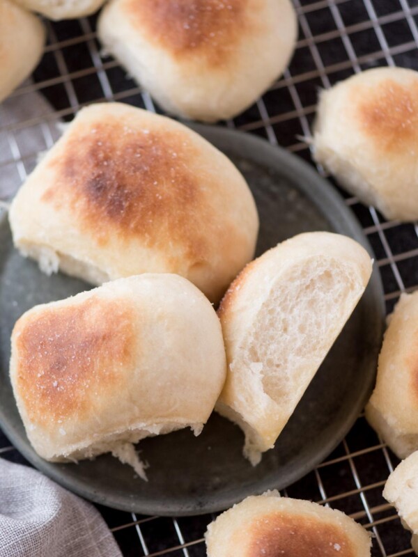 homemade yeast rolls on a plate that is resting on a cooling rack next to a kitchen towel