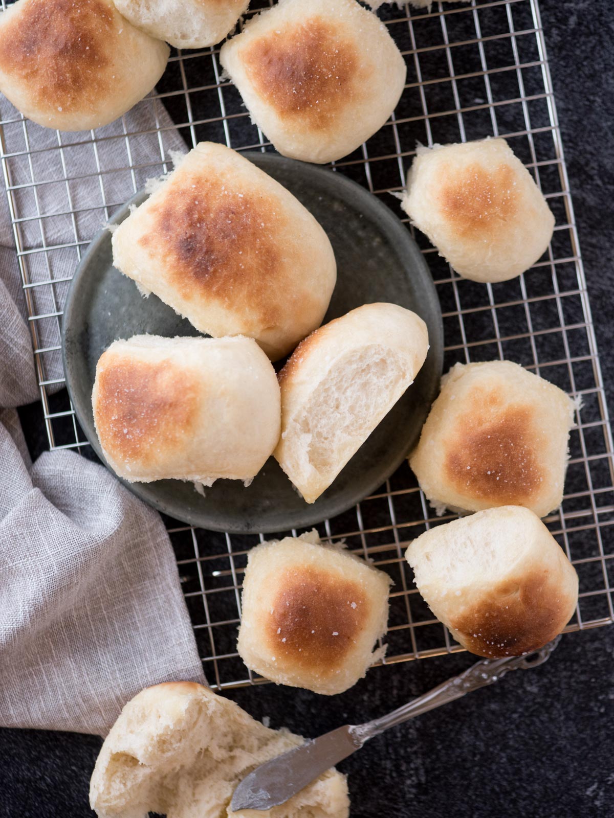 homemade yeast rolls on a cooling rack with a dish towel