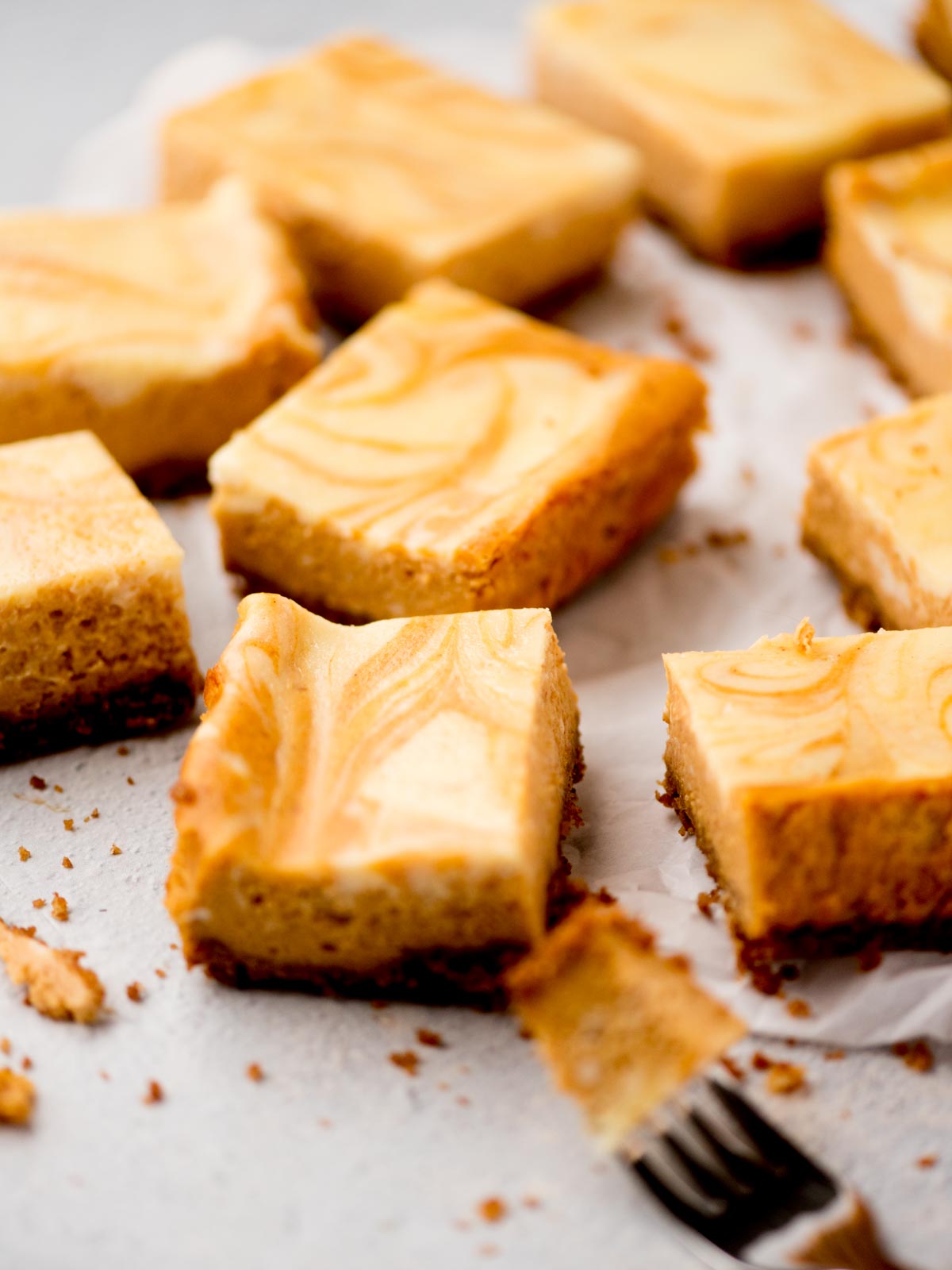 pumpkin cheesecake bars on parchment paper with a bite on a fork
