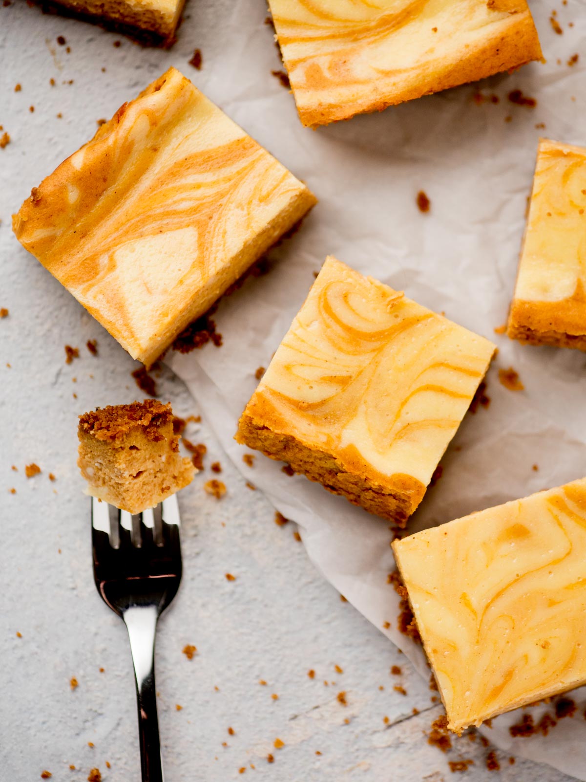 pumpkin cheesecake bars on parchment with a bite on a fork