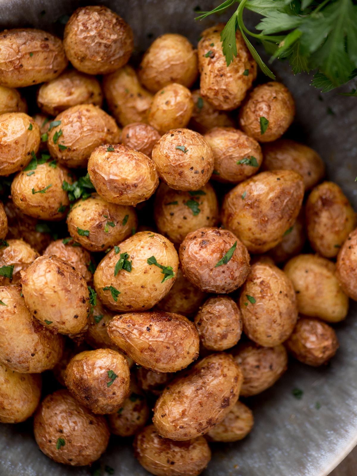 air fried baby potatoes in a bowl topped with fresh parsley. The potatoes are in a bowl surrounded by fresh parsley and a kitchen towel.