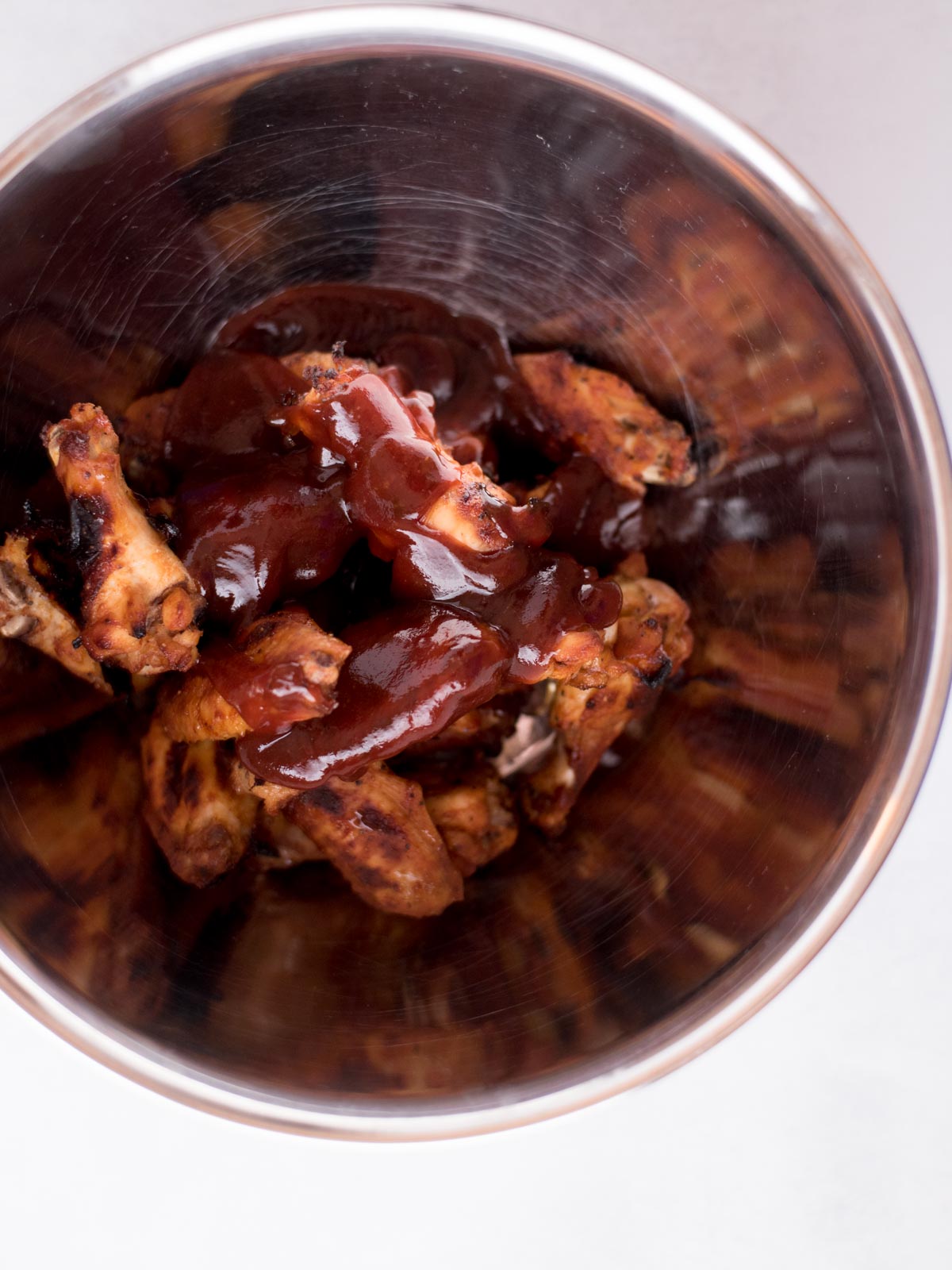 cooked bbq chicken wings in a mixing bowl topped with more barbecue sauce