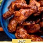 baked bbq chicken wings stacked in a blue bowl surrounded by ranch, fresh celery sticks, and carrot sticks with a text overlay that says "easy oven baked bbq wings"