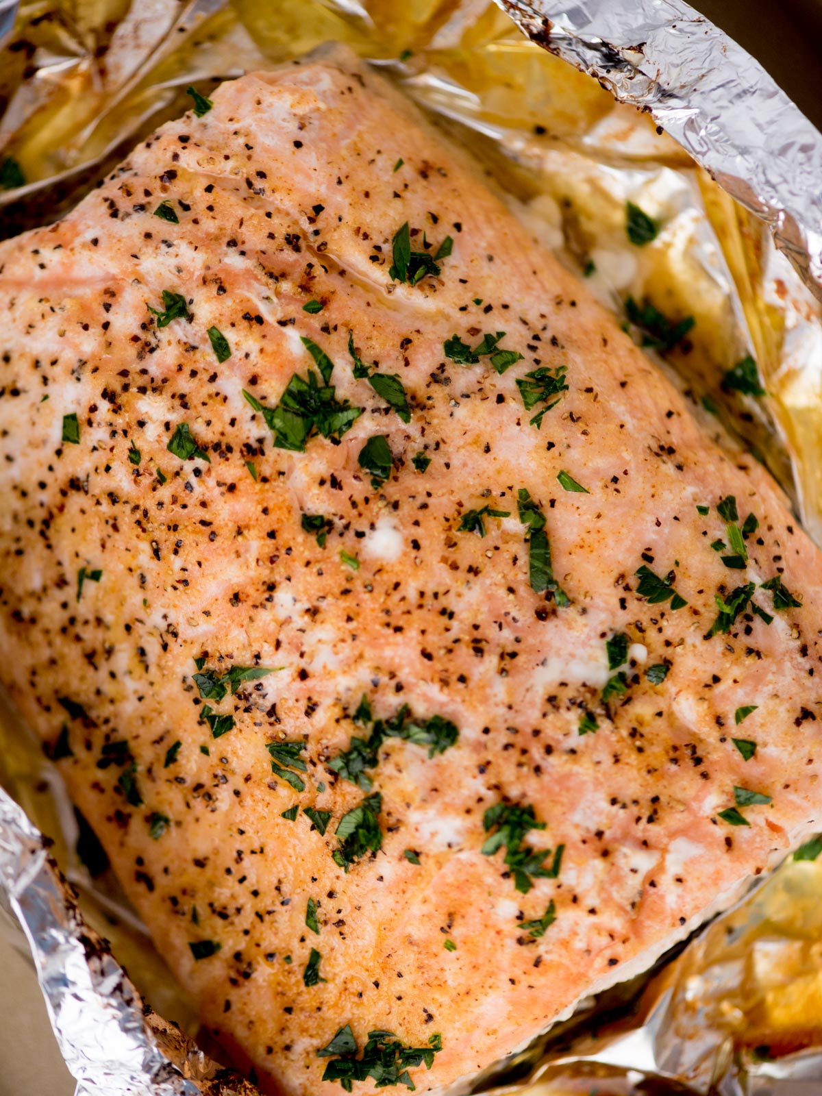 baked salmon in foil on a baking sheet surrounded by fresh parsley and a kitchen towel