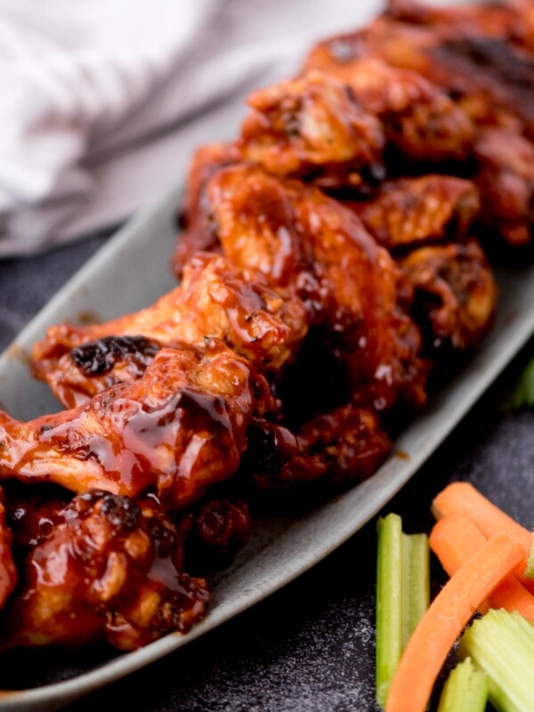 Long oval platter of crockpot bbq chicken wings with fresh veggies laying beside it.