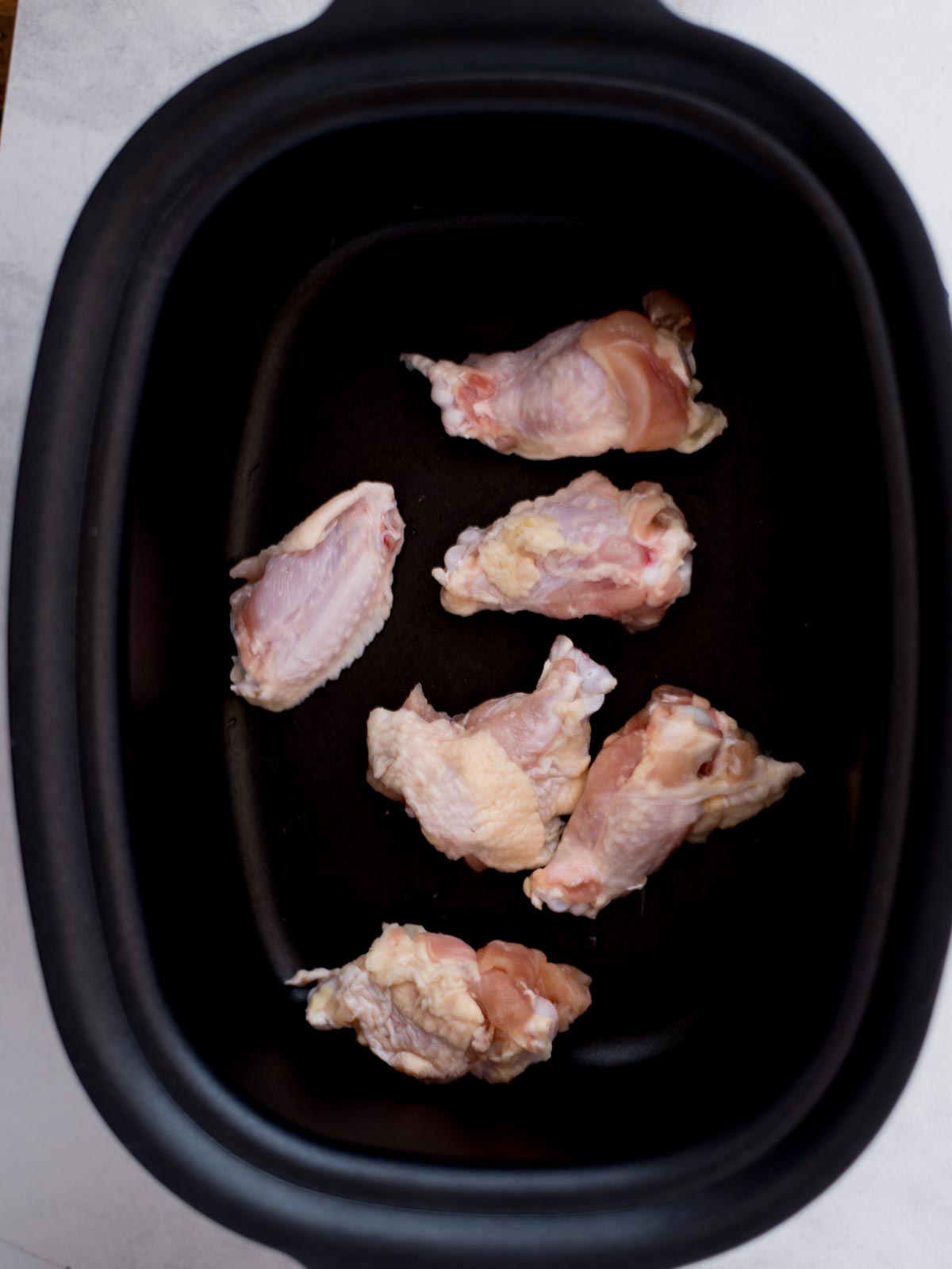 Raw chicken wings laying inside a crockpot.