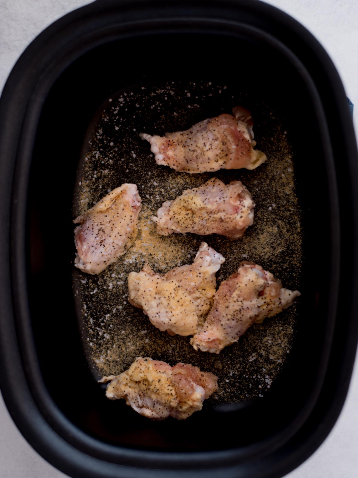 Seasoned raw chicken wings inside a crockpot.