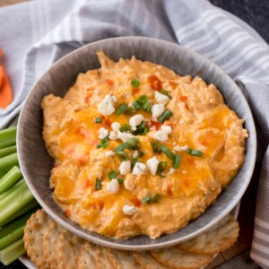 slow cooker buffalo chicken dip topped with sliced green onions, blue cheese, and extra buffalo sauce. Surrounded by crackers and celery.