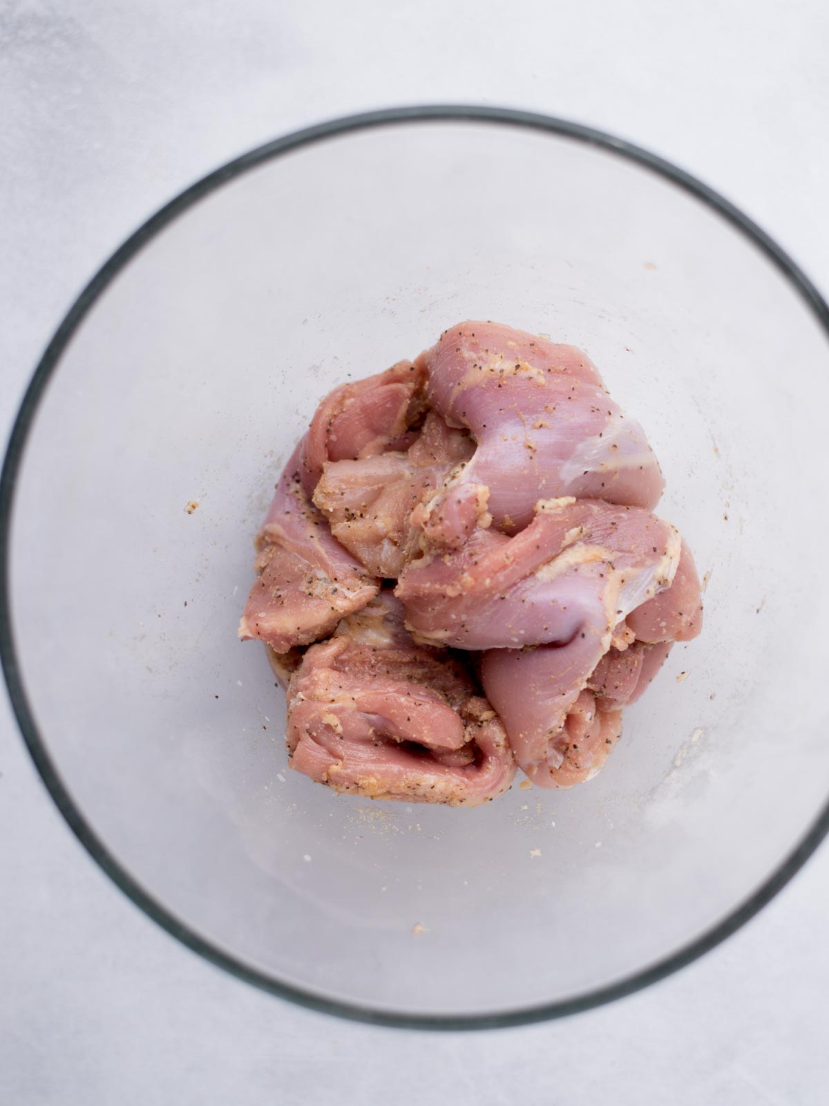 boneless skinless chicken thighs seasoned in a mixing bowl