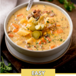 pinterest image with a text overlay that says "easy cheeseburger soup" of cheeseburger soup in a grey bowl with a spoon topped with chopped pickles and cheese. It is on a brown board surrounded by a kitchen towel and fresh parsley.