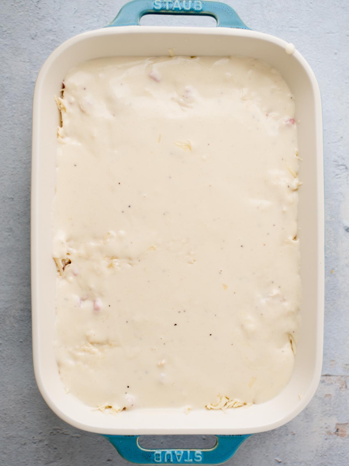chicken cordon bleu casserole assembly where the sauce has been poured over the Swiss cheese