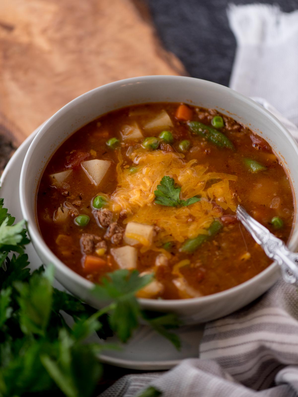 hamburger soup in a grey bowl topped with shredded cheddar cheese and parsley.