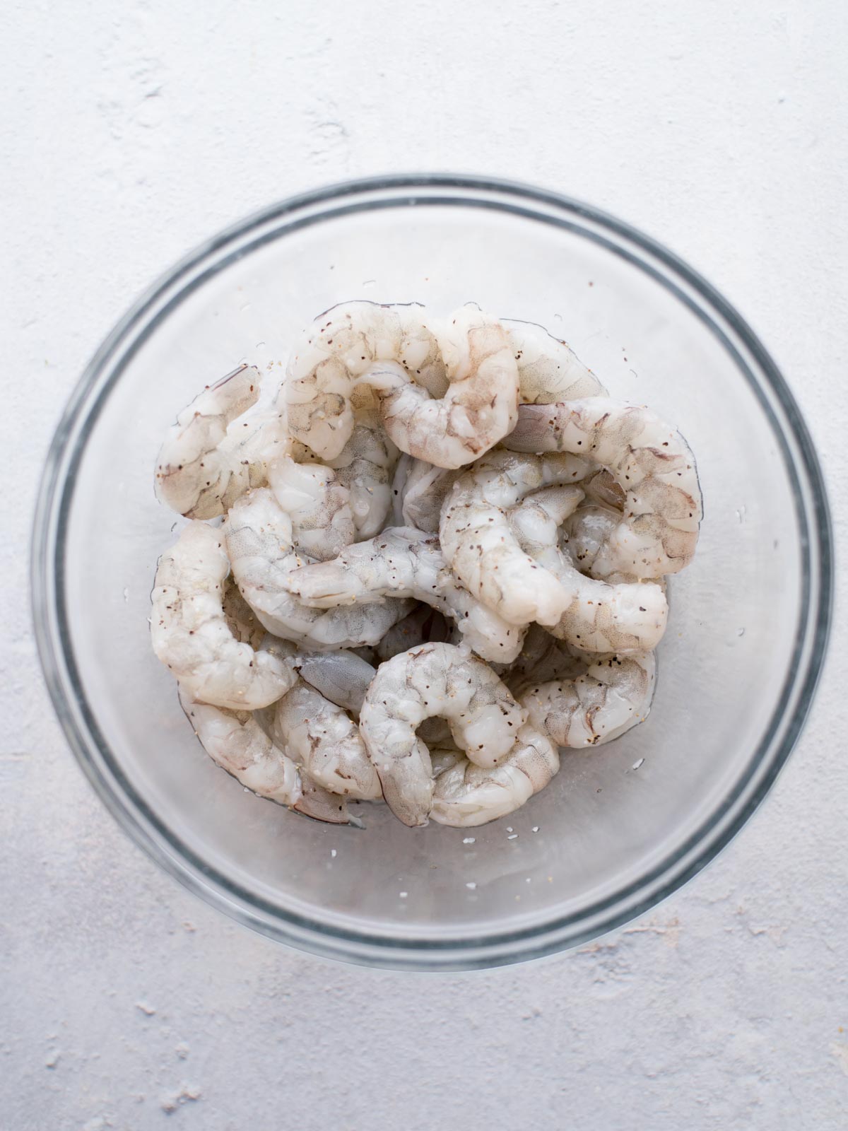 shrimp in a glass mixing bowl seasoned with salt and pepper