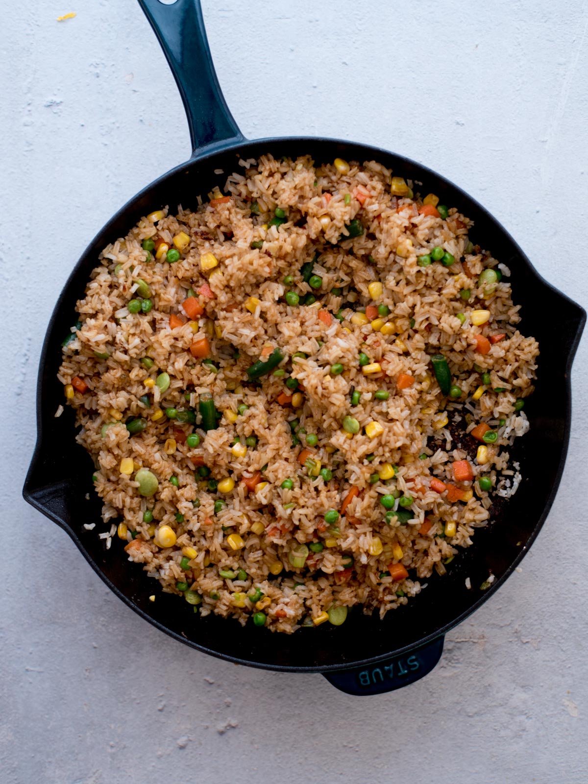 soy sauce coated rice in a skillet with vegetables, garlic, and green onions