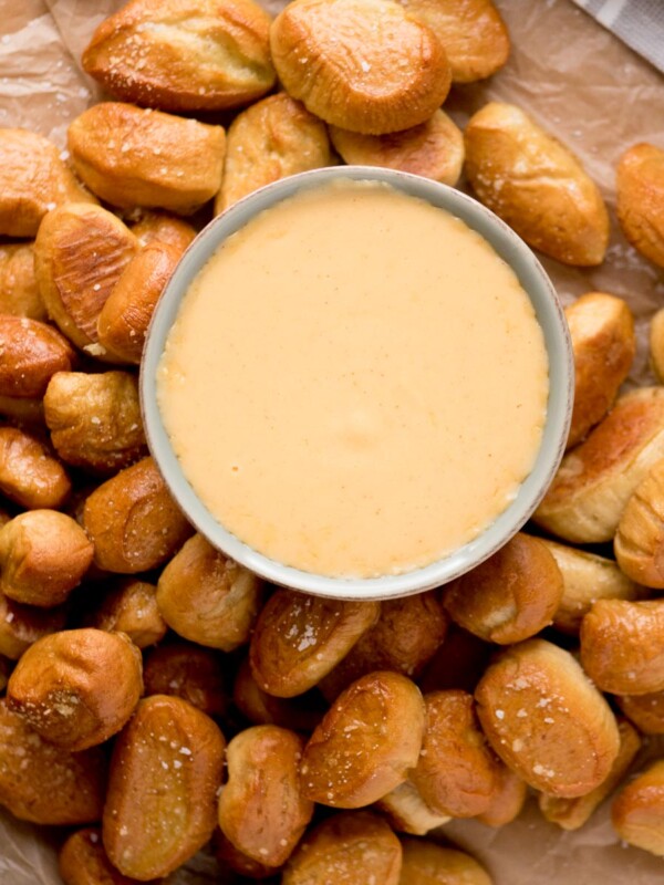 beer cheese dip in a bowl surrounded by soft pretzel bites on parchment paper