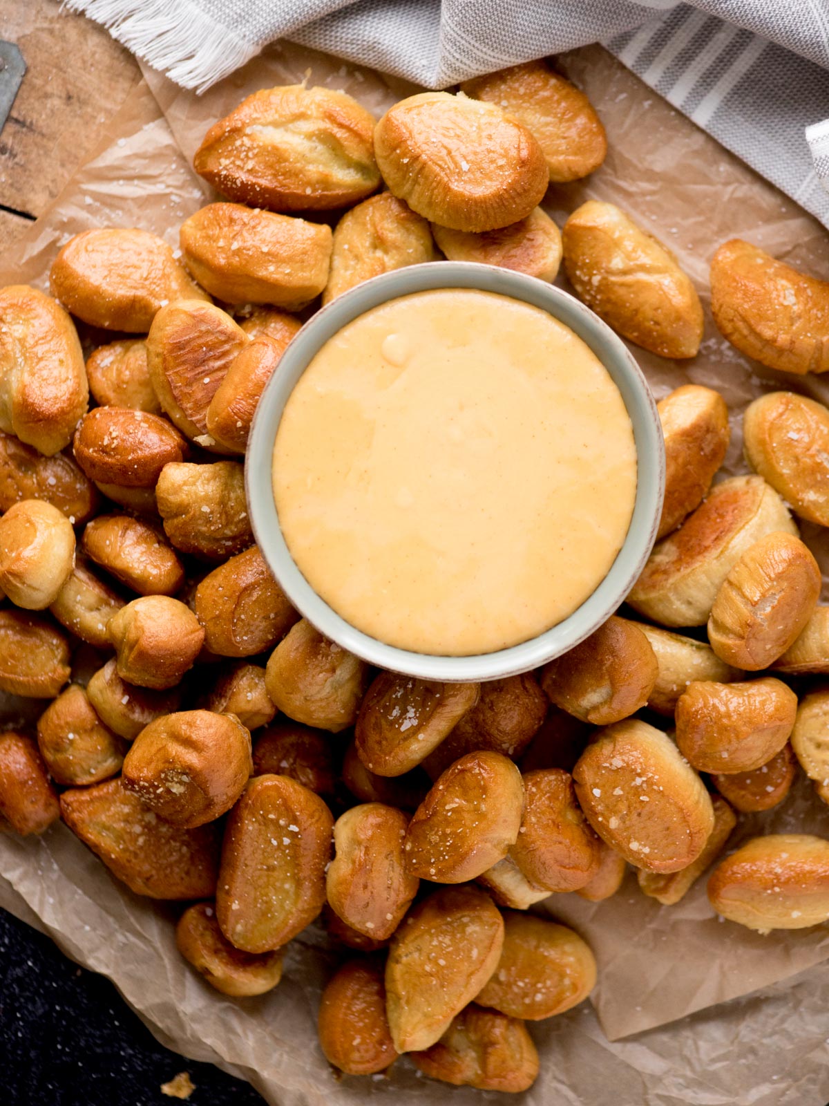 beer cheese dip in a bowl surrounded by pretzel bites on a parchment paper