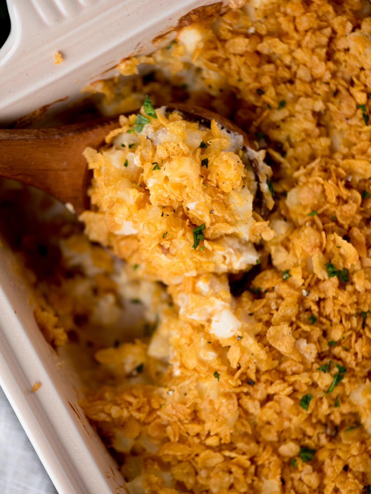 baking dish with funeral potatoes being scooped out with a wooden spoon