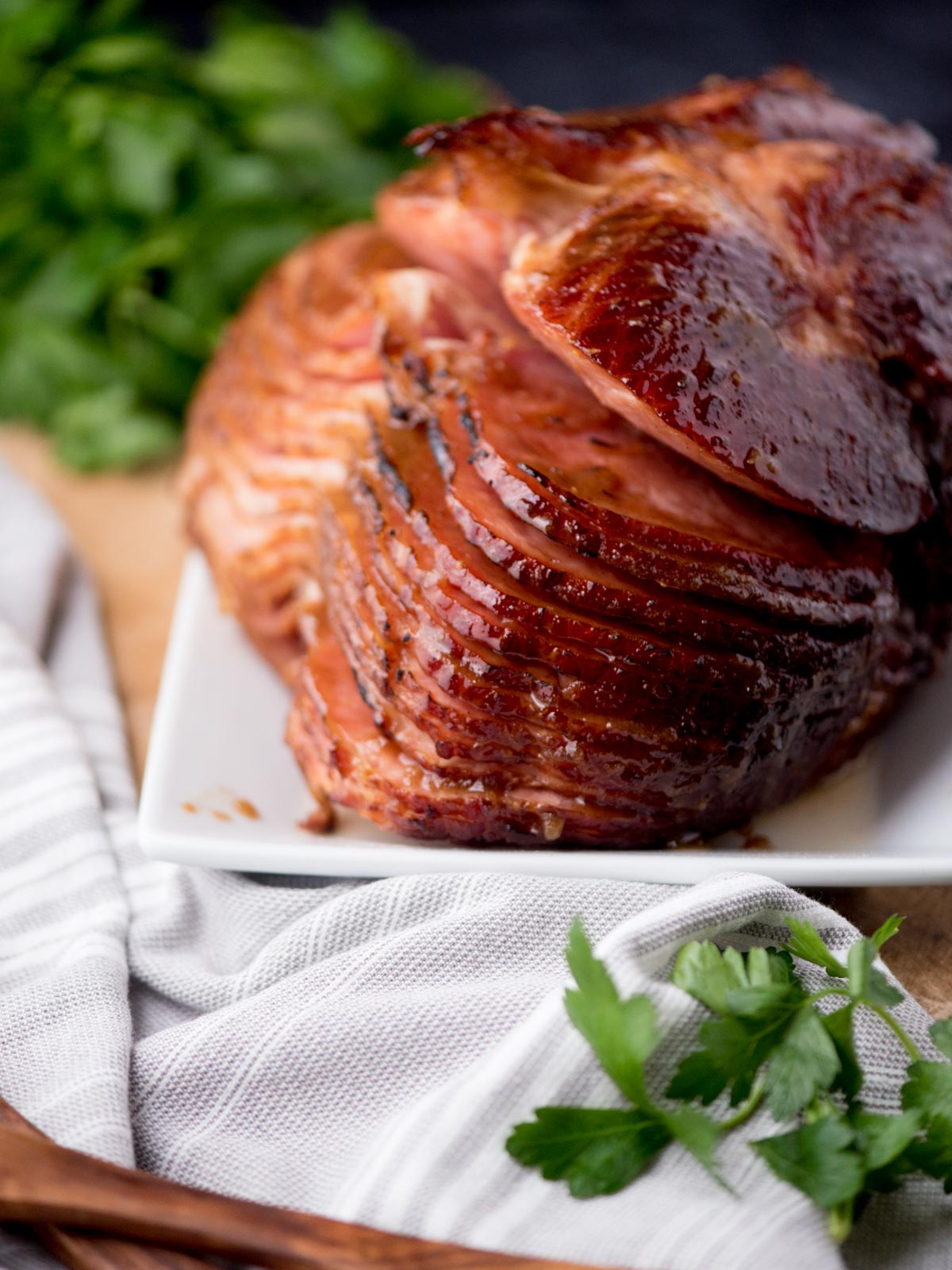 brown sugar glazed ham on a plate surrounded by a kitchen towel and parsley