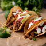 ground beef tacos on parchment paper surrounded by cilantro and limes