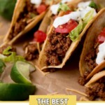 ground beef tacos on parchment paper surrounded by cilantro and limes with a text overlay that says the best ground beef tacos