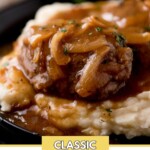 hamburger steak with gravy over a pile of mashed potatoes sitting on a black plate. The plate is on top of a wooden board with parsley in the background. Text on the image says "classic hamburger steak".