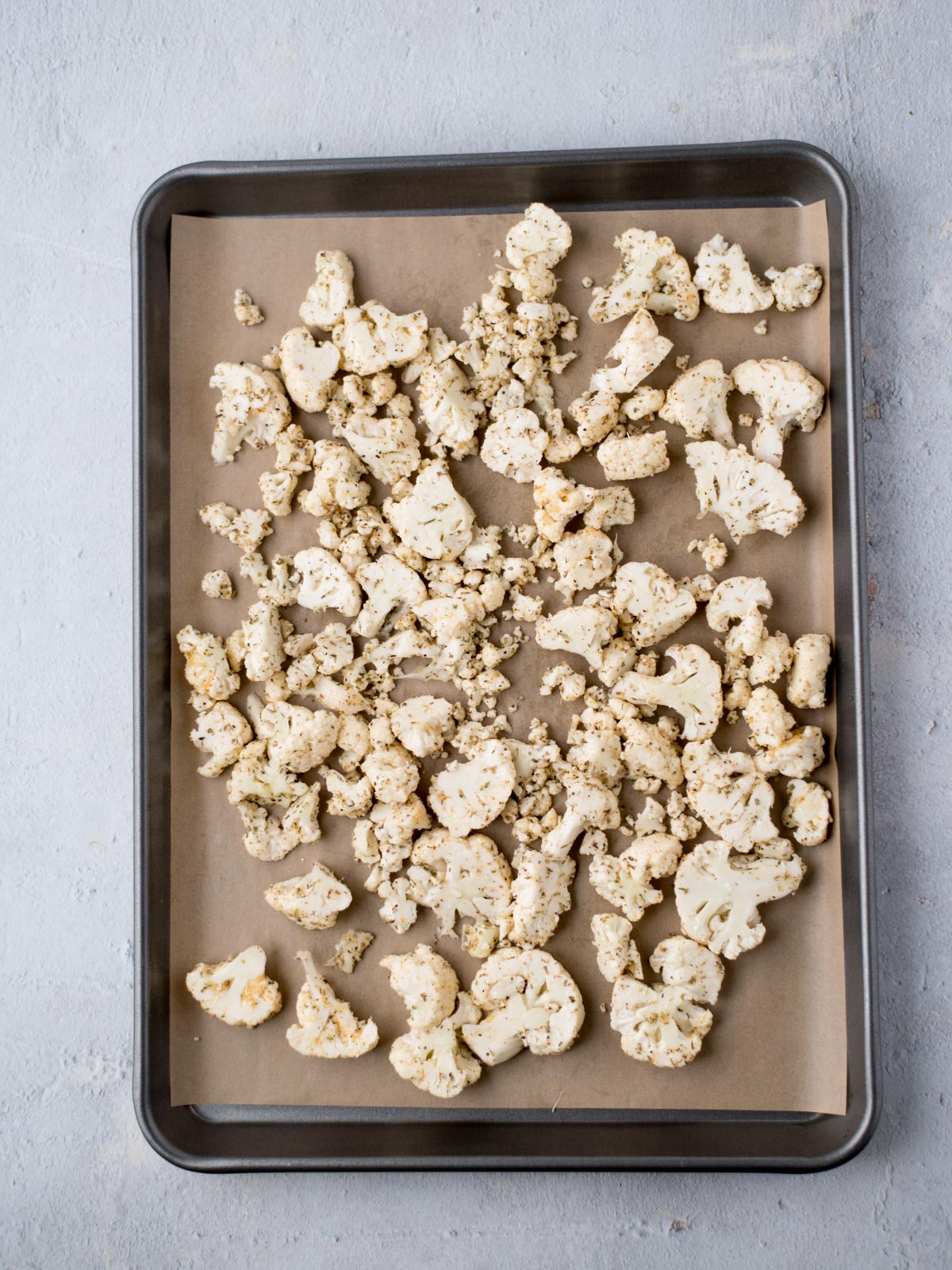 uncooked, seasoned cauliflower on a parchment lined baking sheet