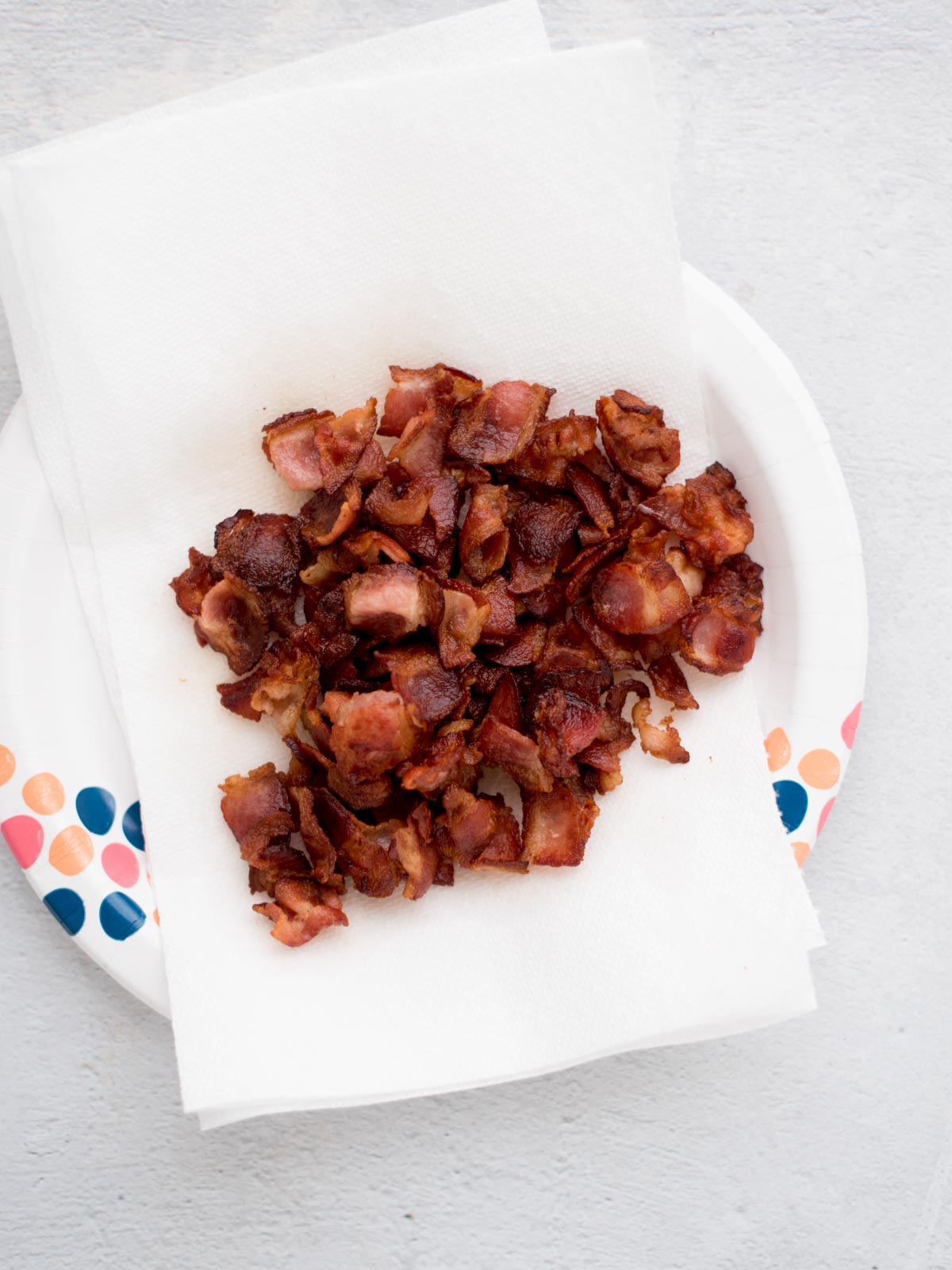 Crispy golden bacon pieces chopped laying on a paper towels covered plate.