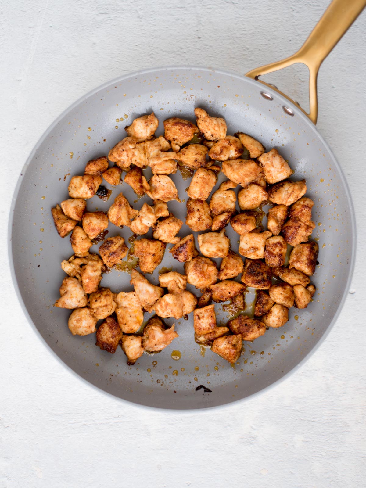 Chicken pieces sauted to a golden brown in a skillet.