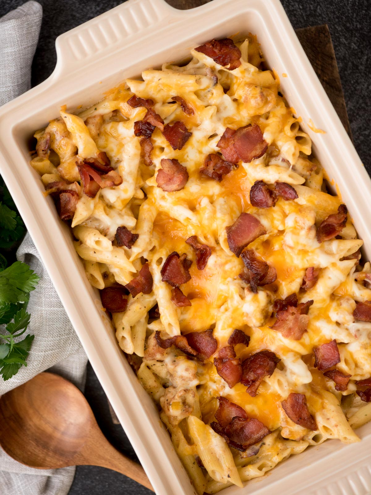 Chicken bacon ranch pasta with melted cheese and bacon over top ready to serve with a wooden spoon resting next to it.