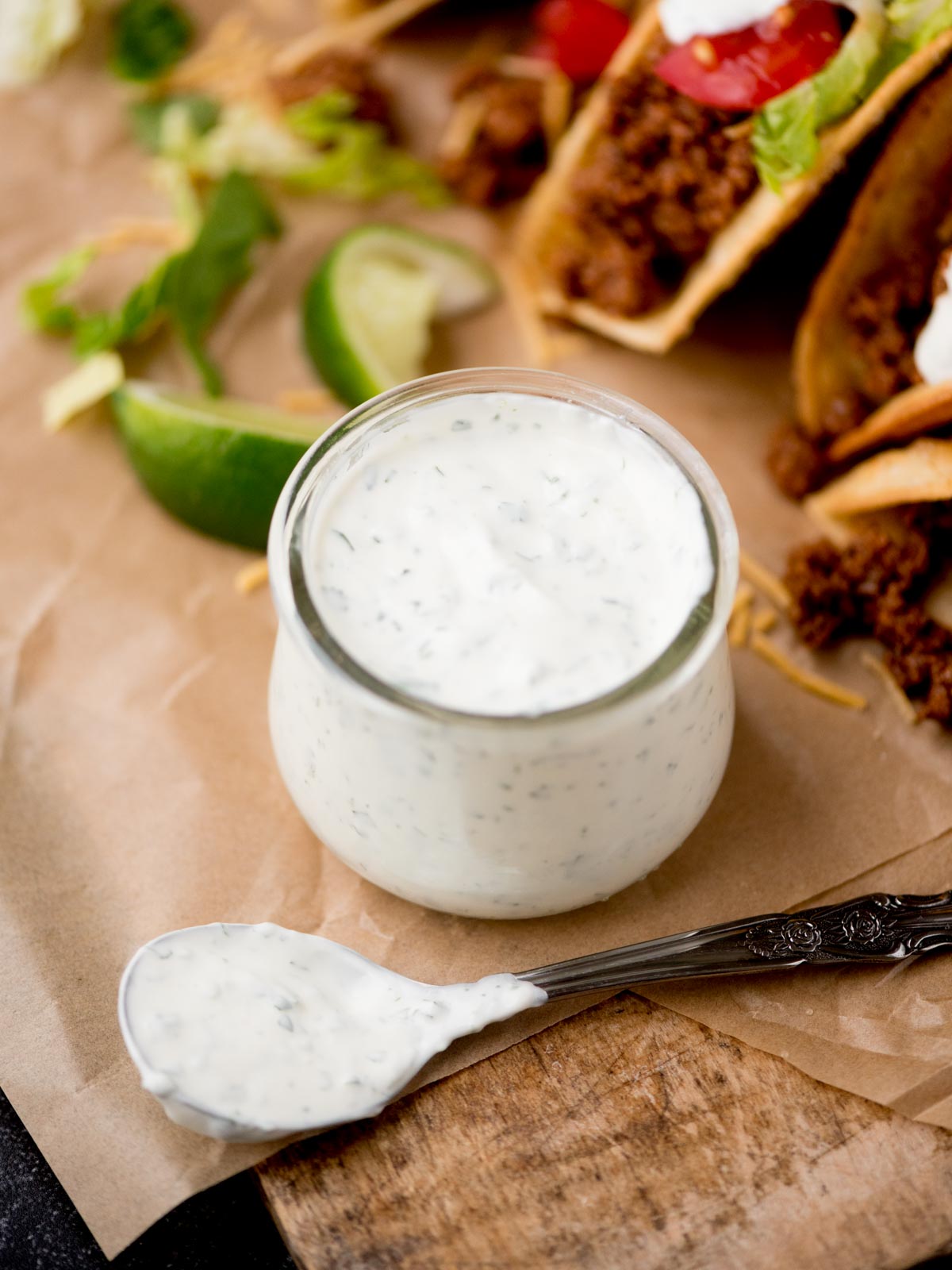 A creamy cilantro lime sauce filling a small glass jar with a spoon covered in the sauce resting next to it.