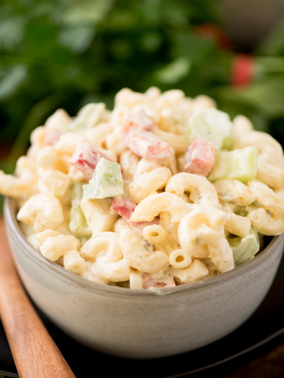 Macaroni salad in a grey bowl surrounded by a serving spoon and fresh parsley.