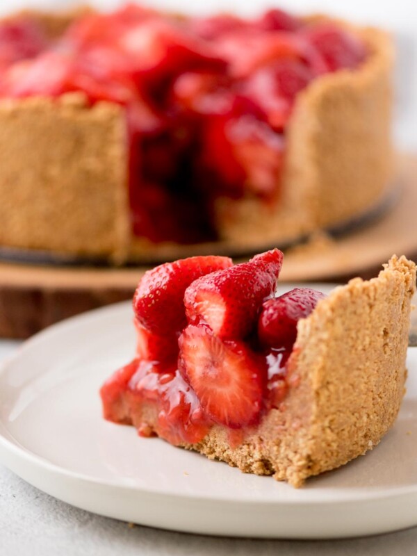 a slice of strawberry pie on a plate with the rest of the pie in the background