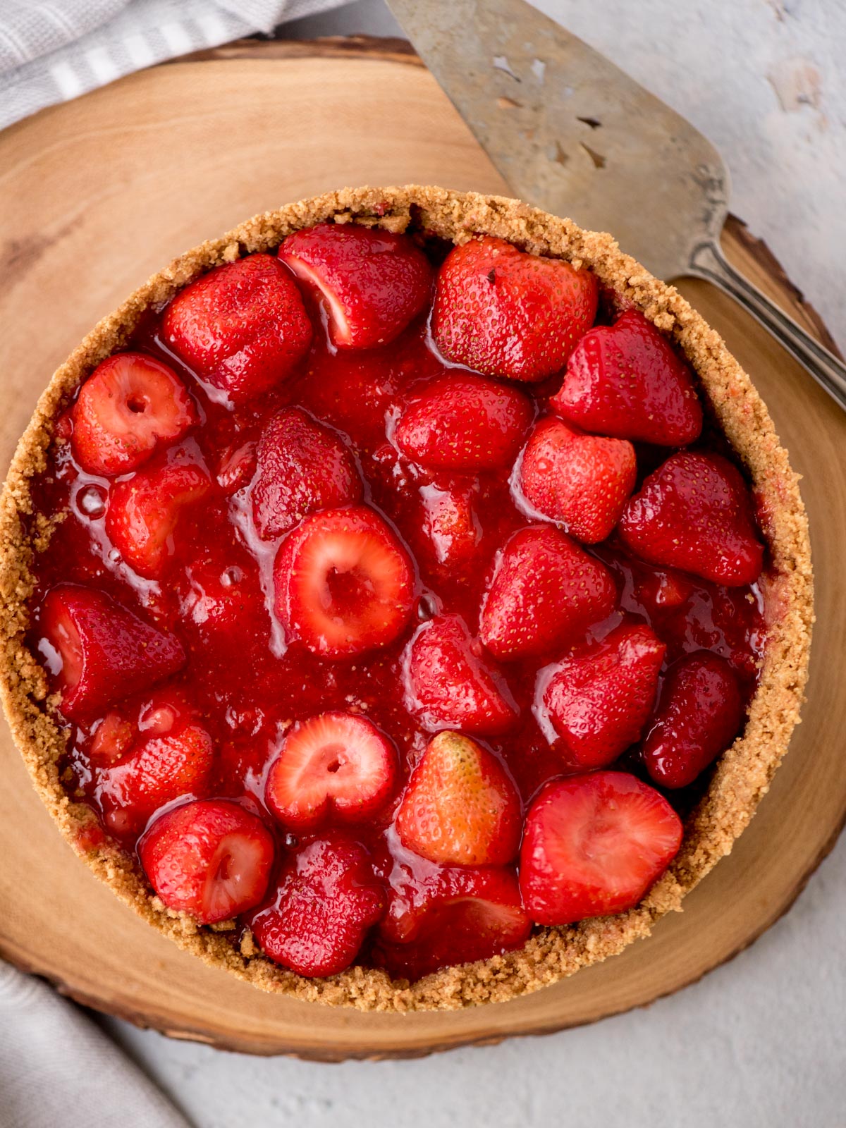 strawberry pie in a graham cracker crust on a wooden stand with a pie utensil next to it