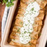 chicken enchiladas in a baking dish topped with sour cream and fresh cilantro