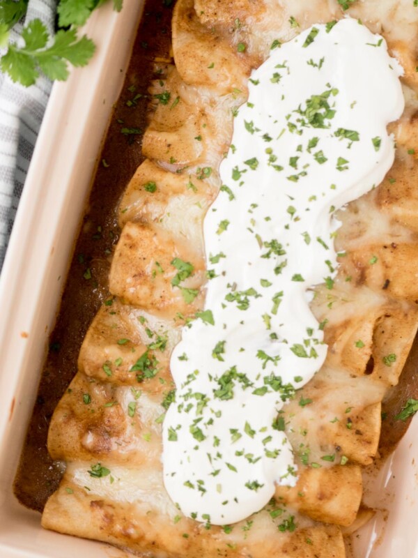 chicken enchiladas in a baking dish topped with sour cream and fresh cilantro