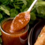 enchilada sauce in a clear jar being scooped out with a spoon