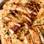 A creamy Cajun chicken pasta dish featuring perfectly seared and sliced chicken breast on top of al dente rigatoni, coated in a rich, creamy sauce and garnished with fresh parsley