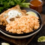 spanish rice on a plate with enchiladas topped with chopped cilantro on a wooden board
