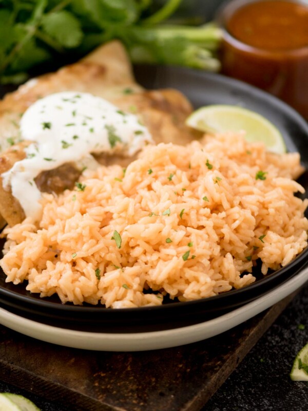 spanish rice on a plate with enchiladas topped with chopped cilantro on a wooden board