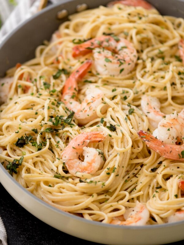 A pan filled with creamy shrimp linguine, featuring perfectly cooked shrimp scattered throughout. The dish is garnished with chopped herbs and appears rich and flavorful. Utensils and a striped napkin are partially visible beside the pan, completing this inviting shrimp pasta scene.