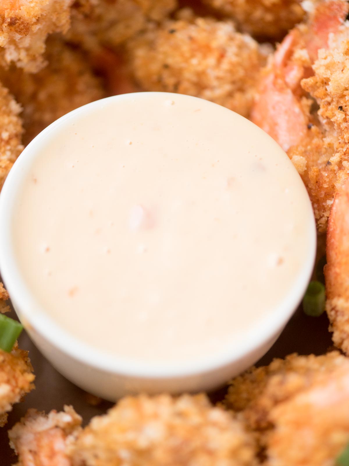 Close-up of a creamy dipping sauce in a white bowl surrounded by breaded fried shrimp. The sauce is pale and smooth, while the shrimp are golden brown and crispy, suggesting a savory appetizer or seafood meal.