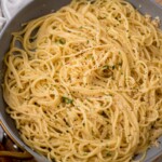A skillet filled with spaghetti pasta tossed in a creamy, lemon garlic cheese sauce, topped with freshly ground black pepper and garnished with chopped parsley.